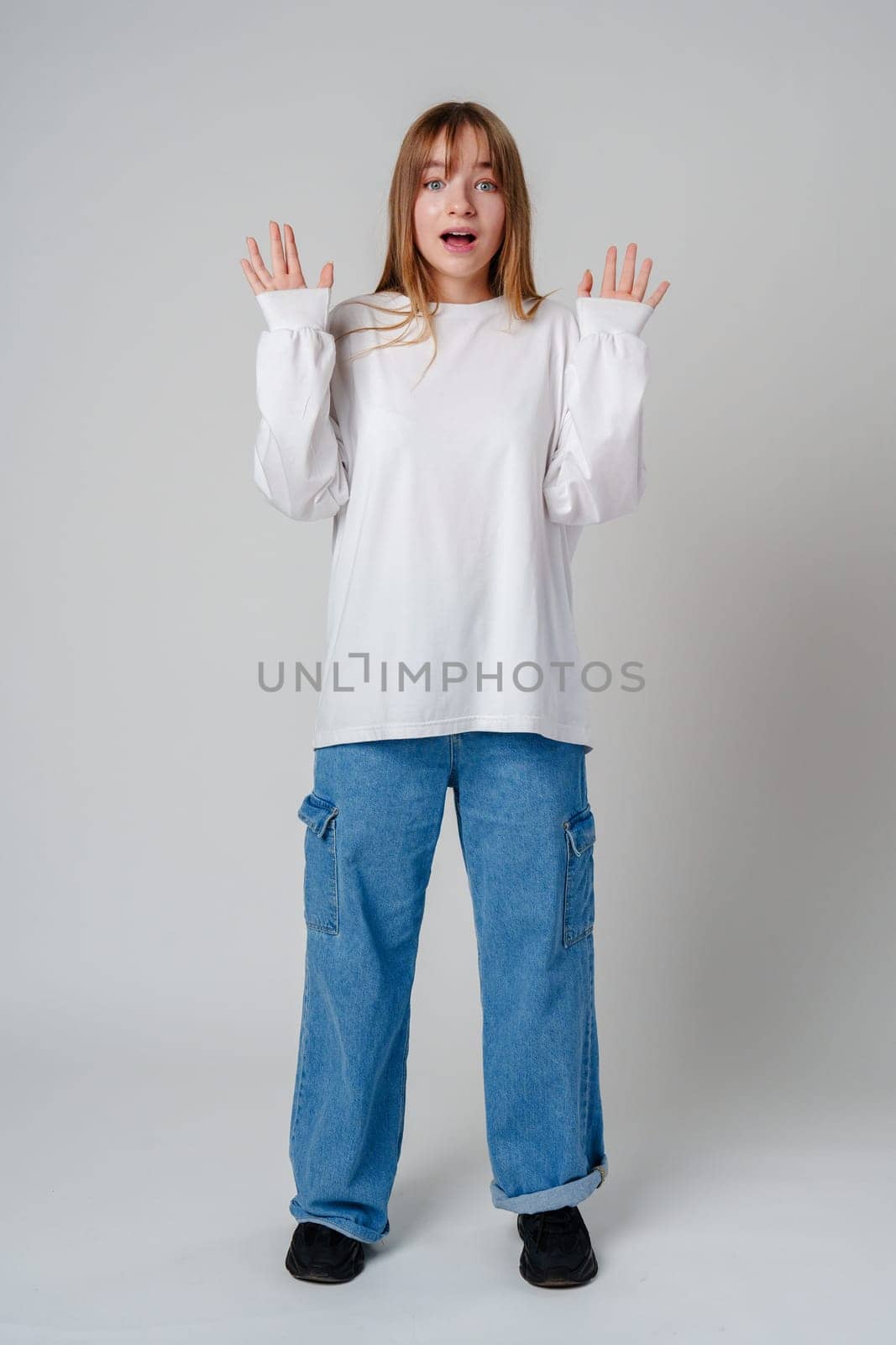 A surprised child wearing a white long-sleeve shirt and blue jeans expresses confusion in a studio setting close up