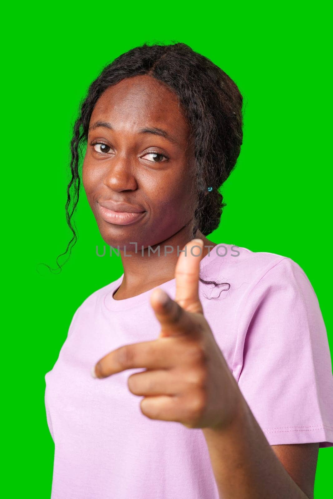 Young woman in a pink shirt playfully pointing fingers at the camera against a bright green background in studio