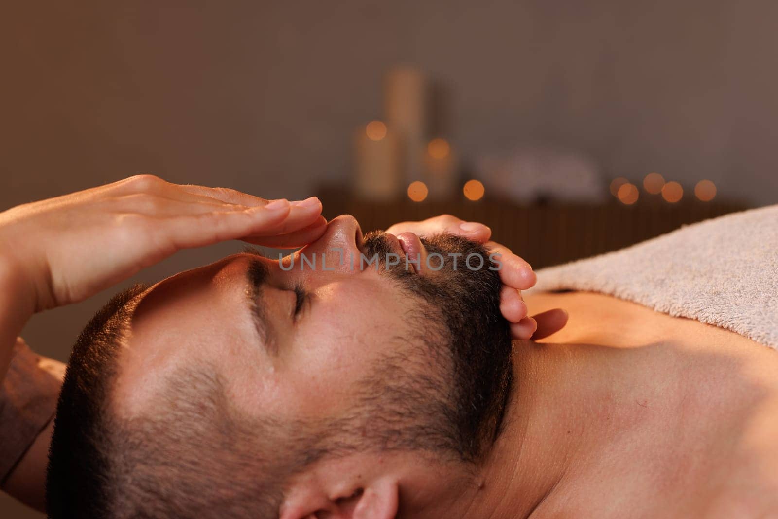 Close-up of female massage therapist's hands massaging man's forehead on dark background, effective facial massage for wrinkles, rejuvenation