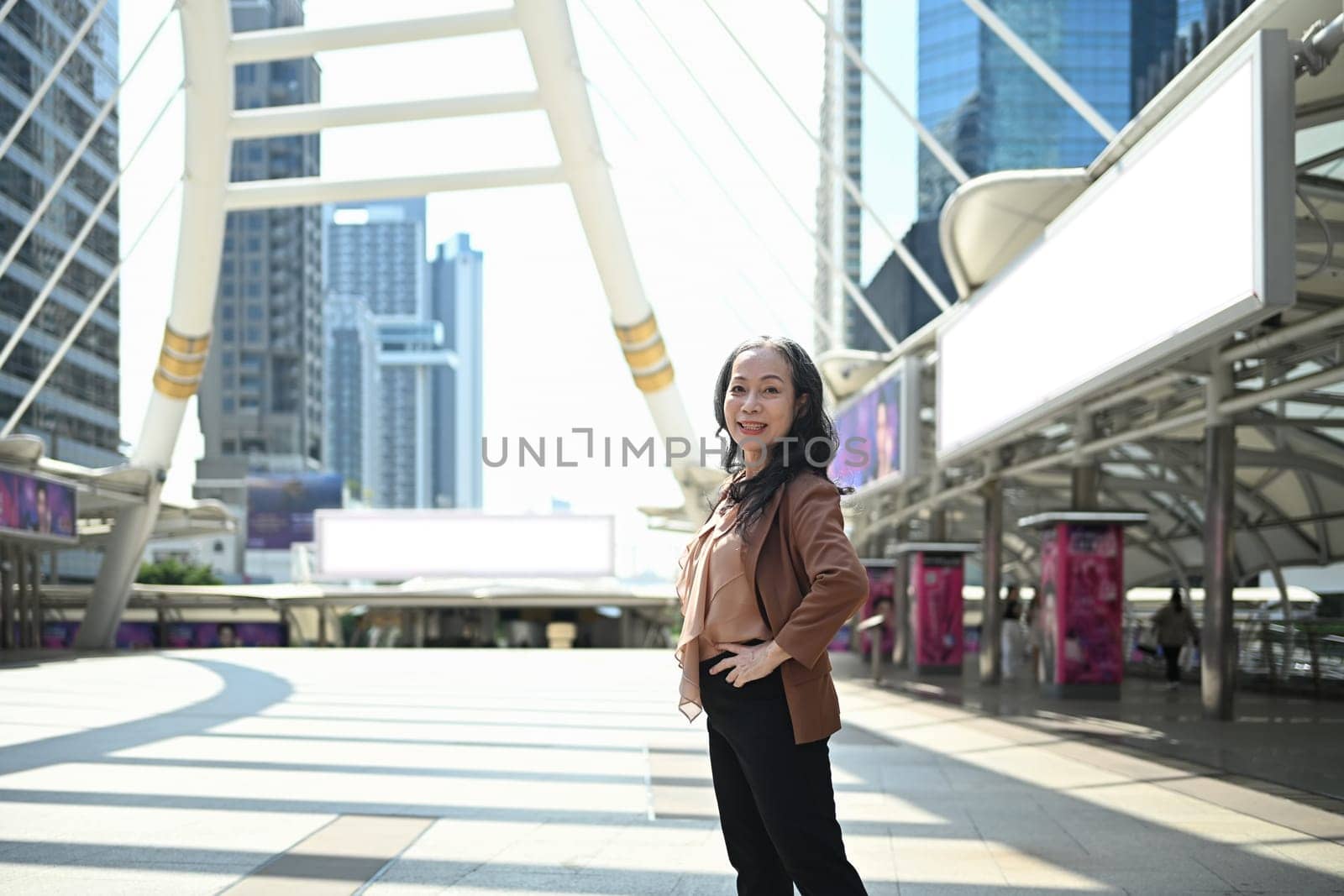 Confident mature businesswoman posing in modern cityscape.