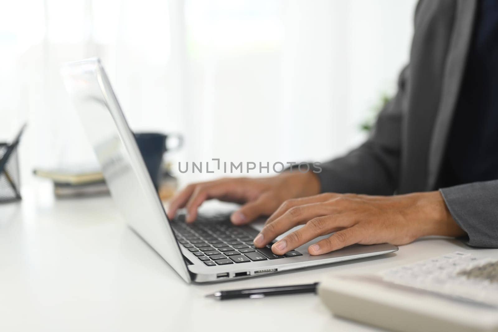 Close up of businessman typing on keyboard in modern workspace.