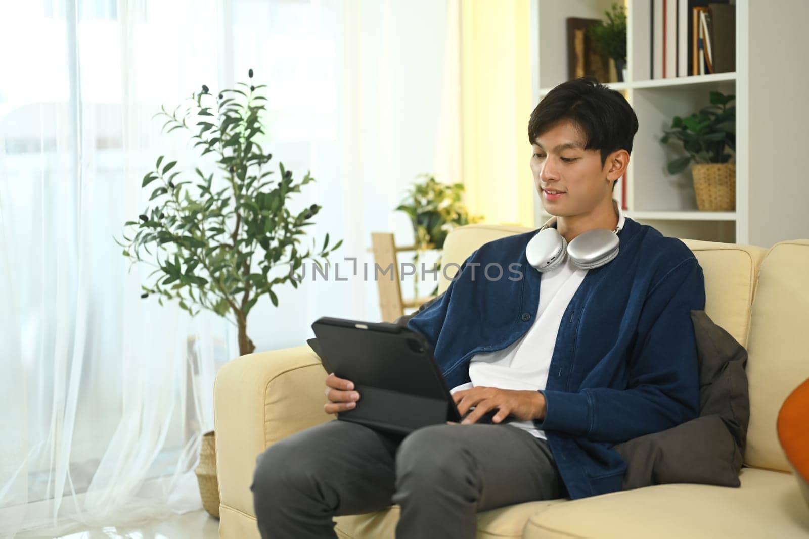 Handsome young asian man using digital tablet on a sofa at home.