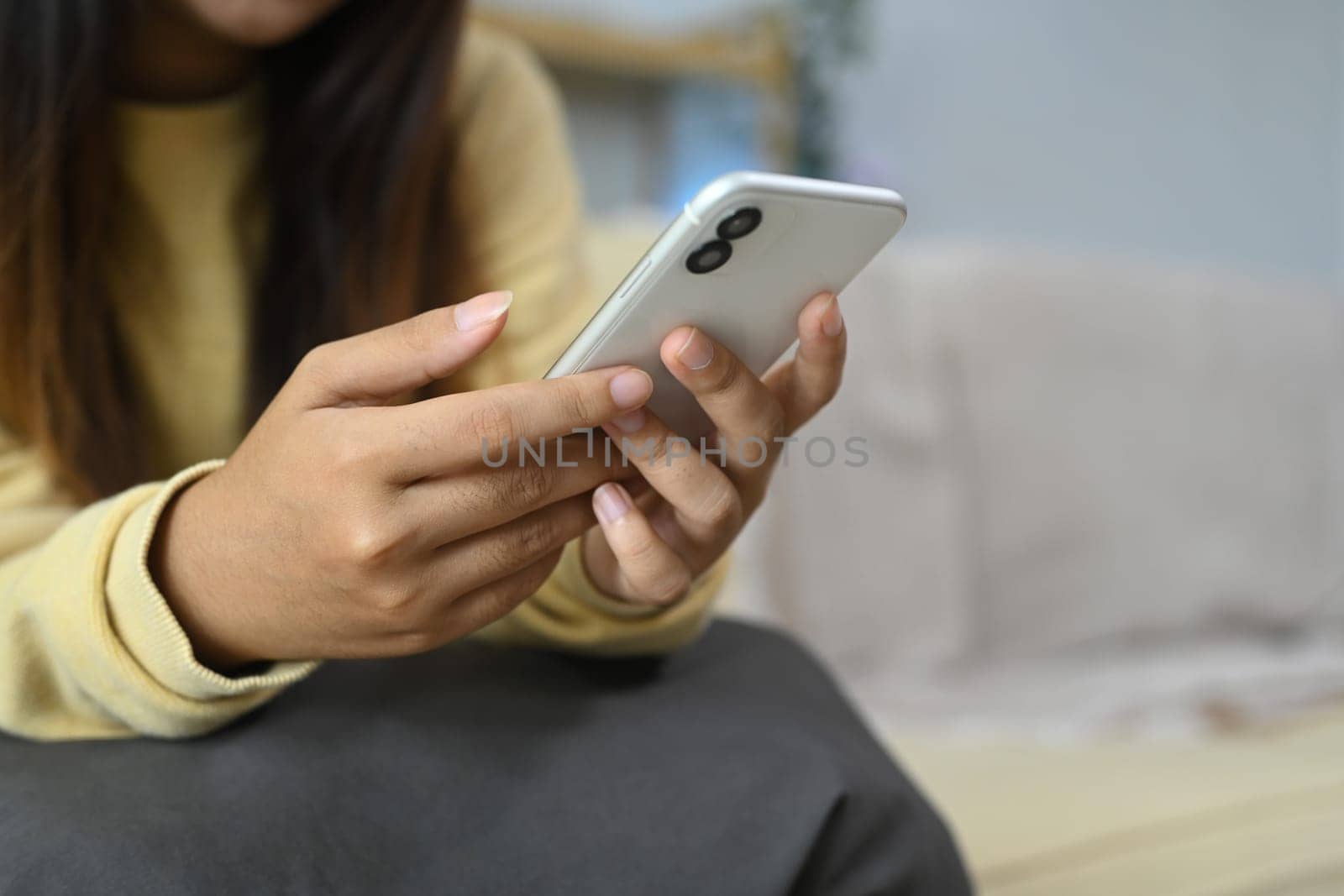 Young woman typing text message on mobile phone and relaxing on couch at home.
