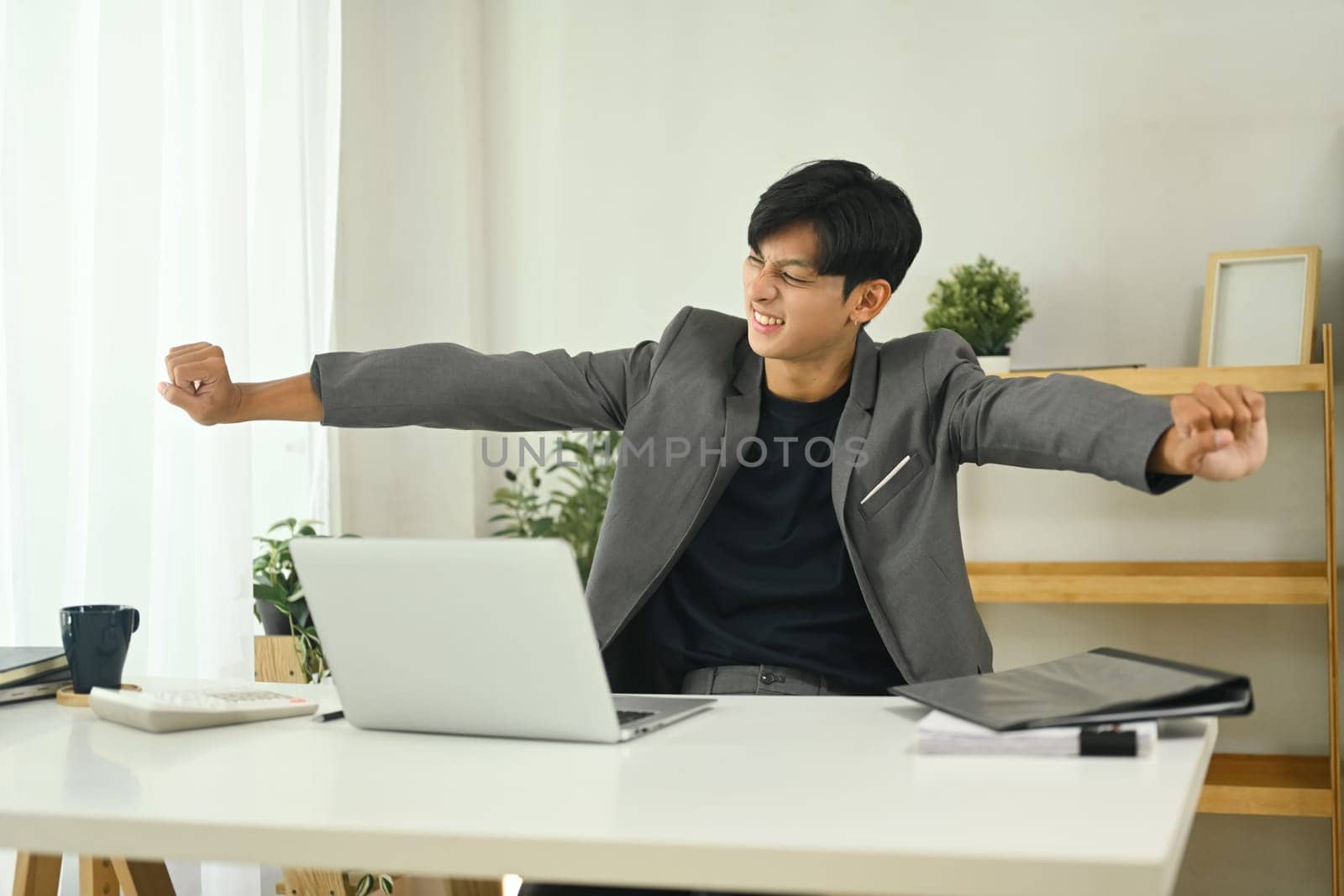 Young businessman relaxing and stretching after long work session in the office.