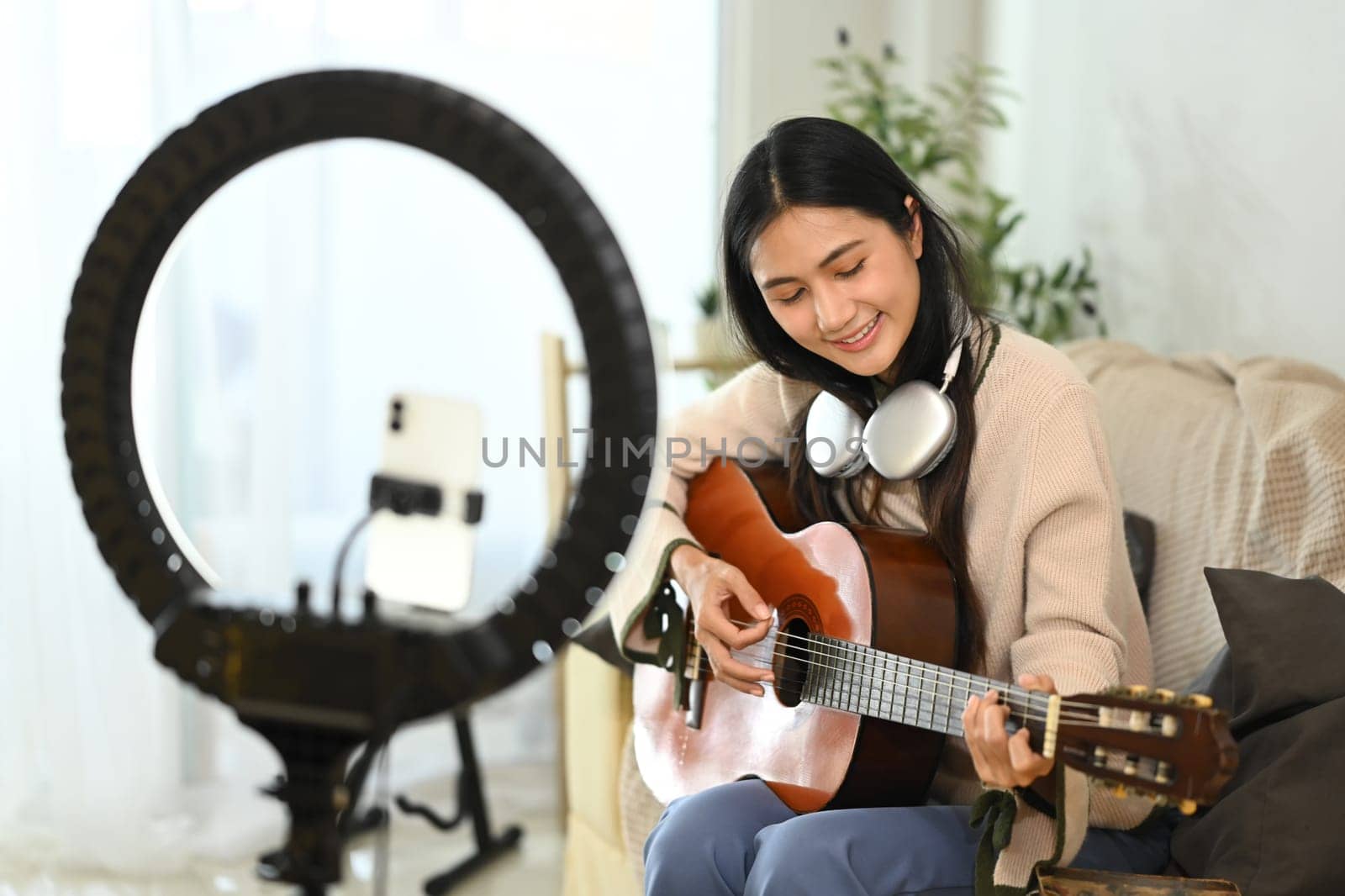 Smiling female music influencer recording video tutorial on playing guitar.
