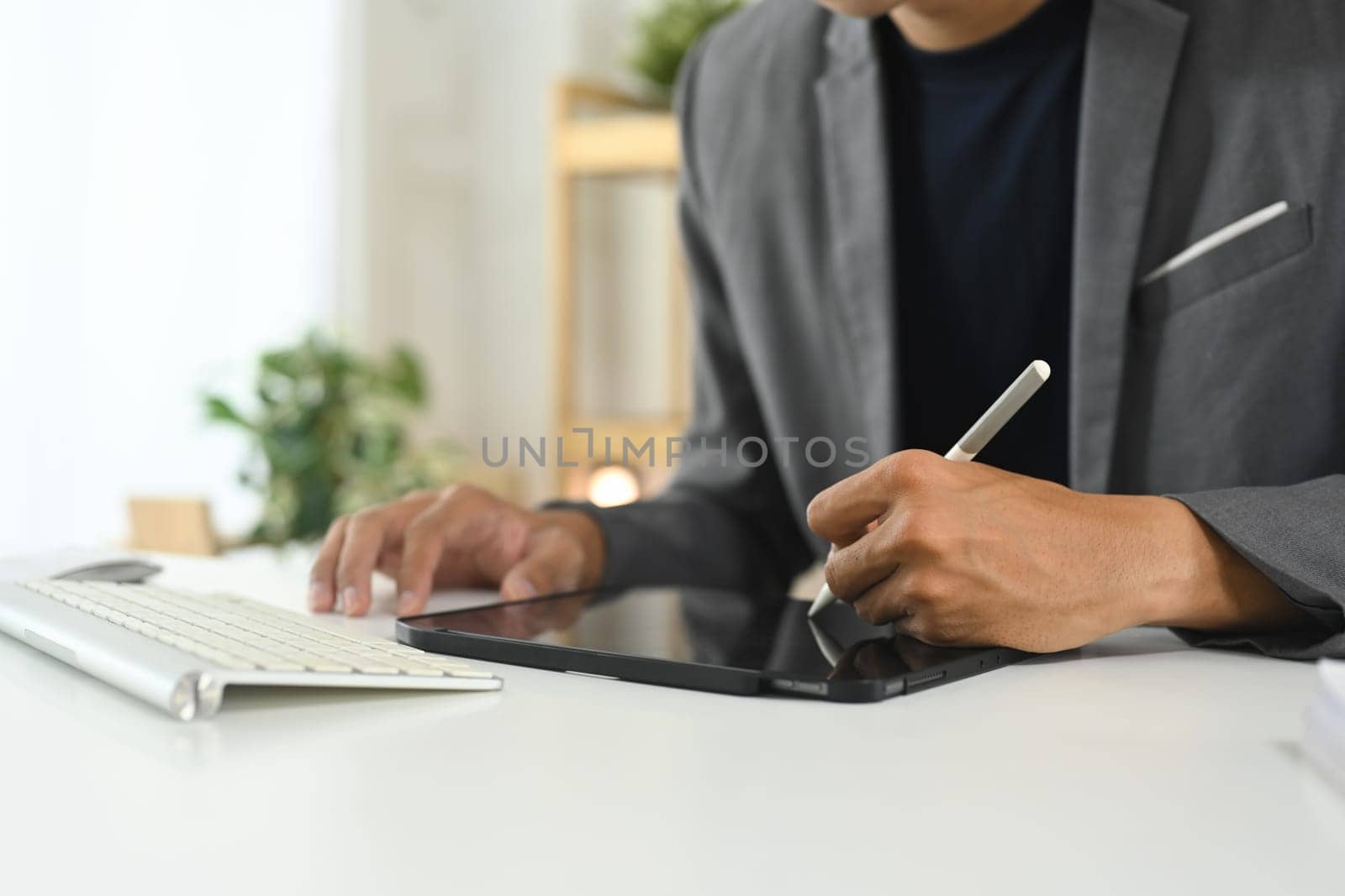Cropped shot businessman in suit working on digital tablet with stylus pen in bright workspace.