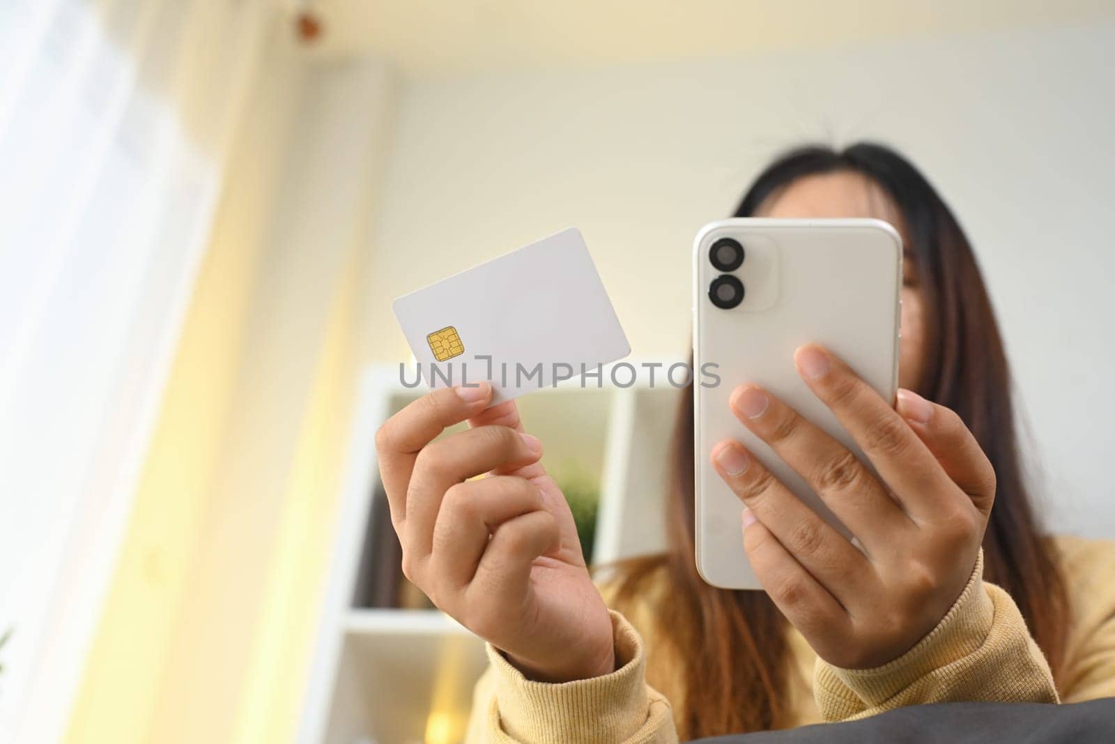 Cropped short happy young woman making online transaction at home with mobile application.