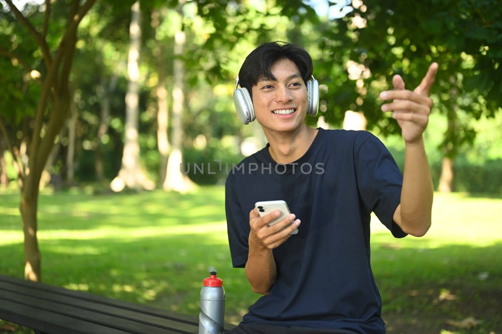 Smiling young sports man resting after training outdoors and using mobile phone.