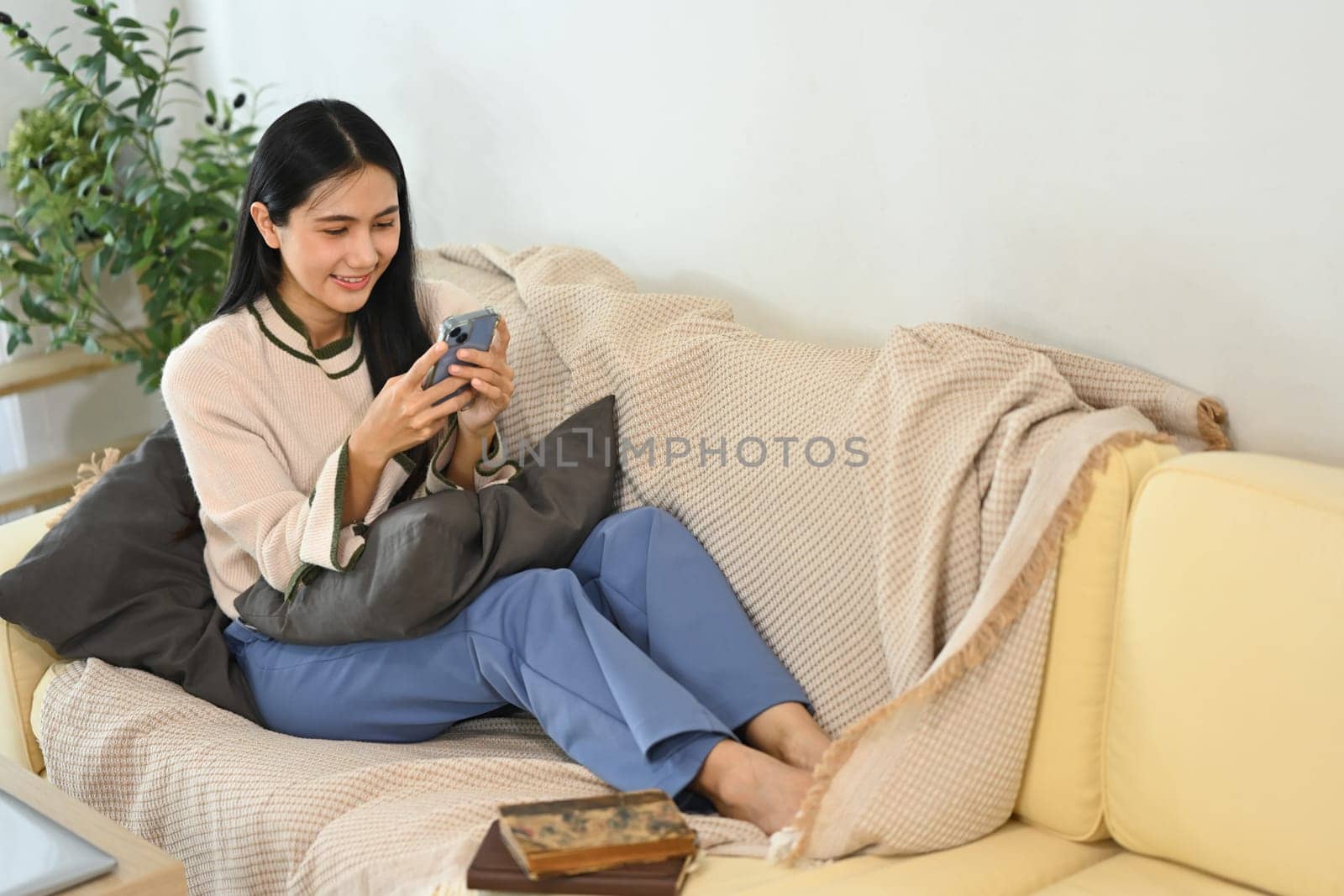 Smiling young woman sitting in living room and checking messages on her mobile phone.