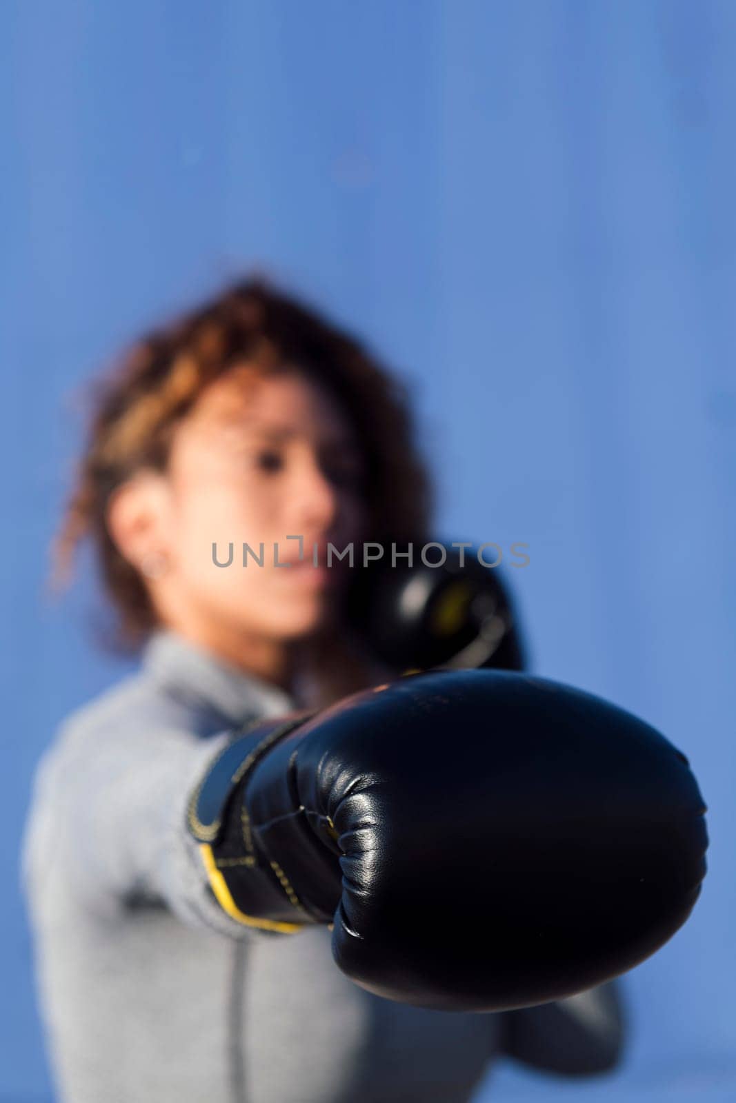 unrecognizable adult female boxer ready to fight on boxing gloves during workout on blue background, concept of strength and healthy lifestyle, selective focus