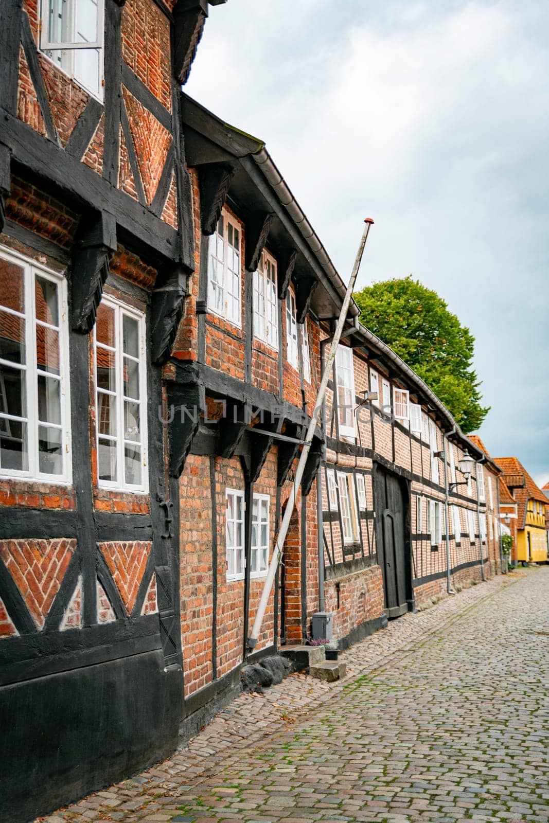 A picturesque view of traditional half-timbered houses lining an old cobblestone streetin ebeltoft in denmark, evoking a sense of history and European charm. The overcast sky adds a serene atmosphere.