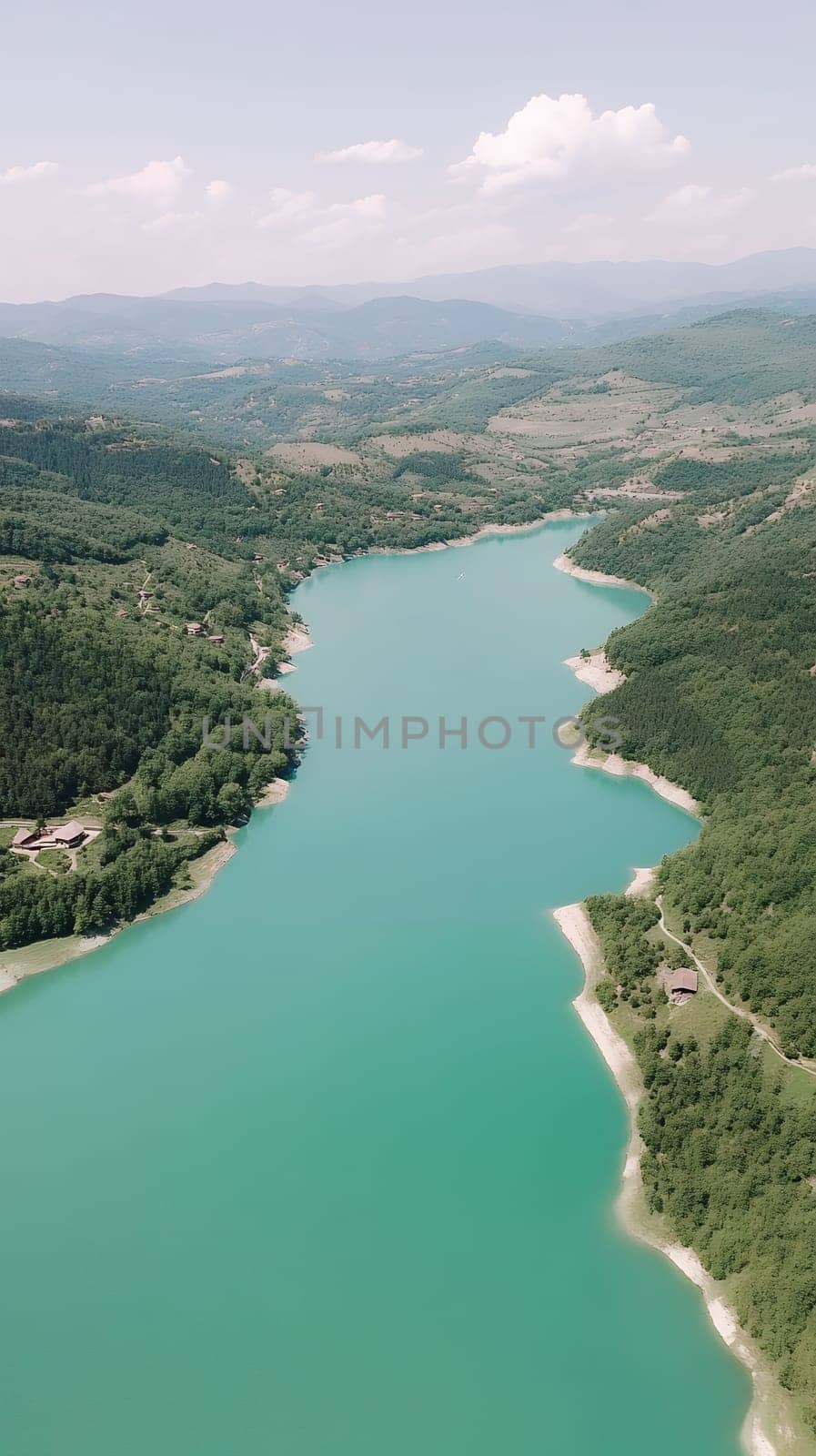 Aerial view of a serene turquoise lake surrounded by lush green hills under a clear sky.
