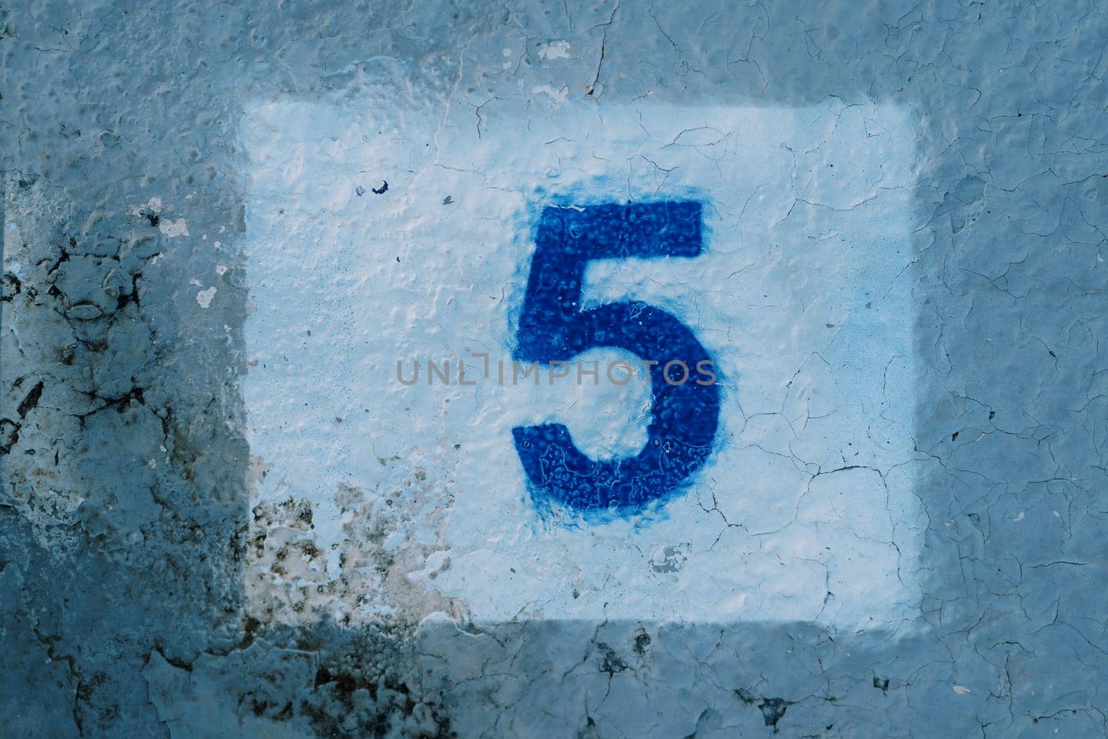 Number five painted on a blue mud-stained wall in a white rectangle. High quality photo