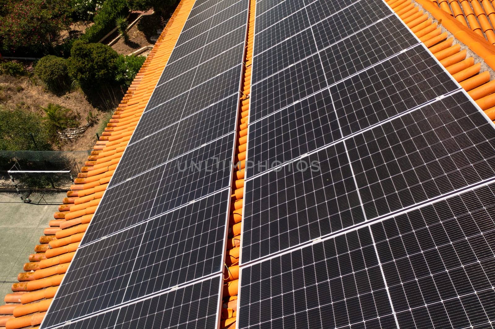 Drone capturing solar panels on house rooftop in city. Residential structure is equipped with green renewable energy generators.