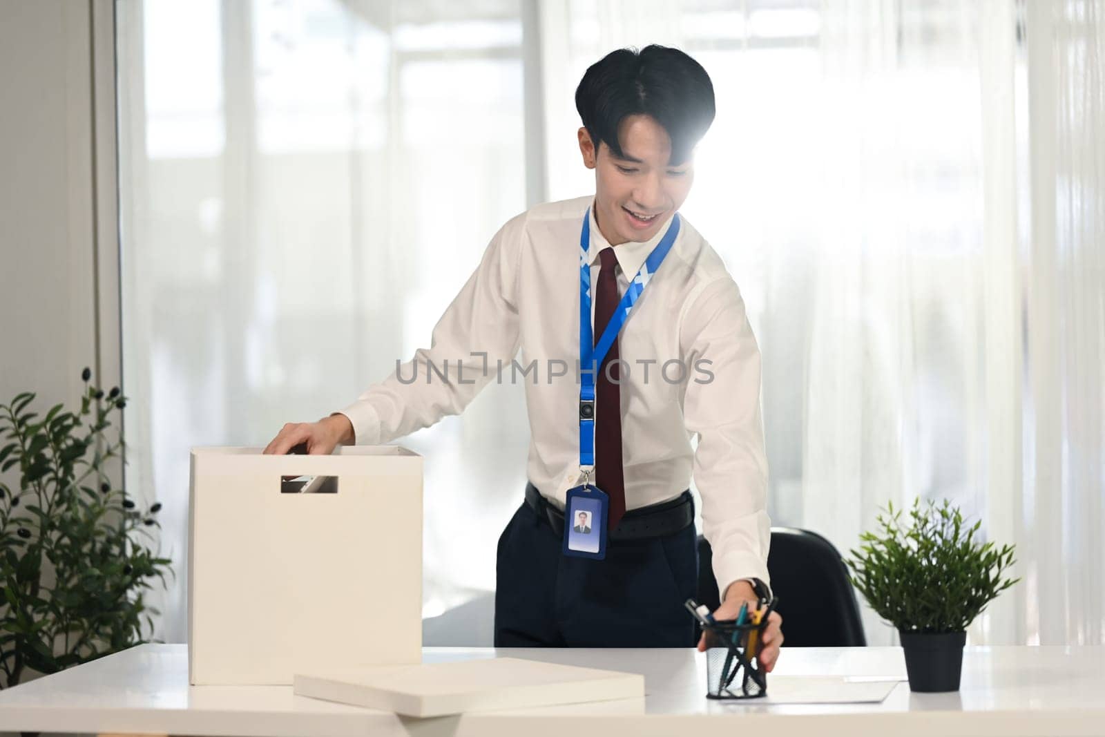 Smiling employee organizing desk supplies in office after getting hired.