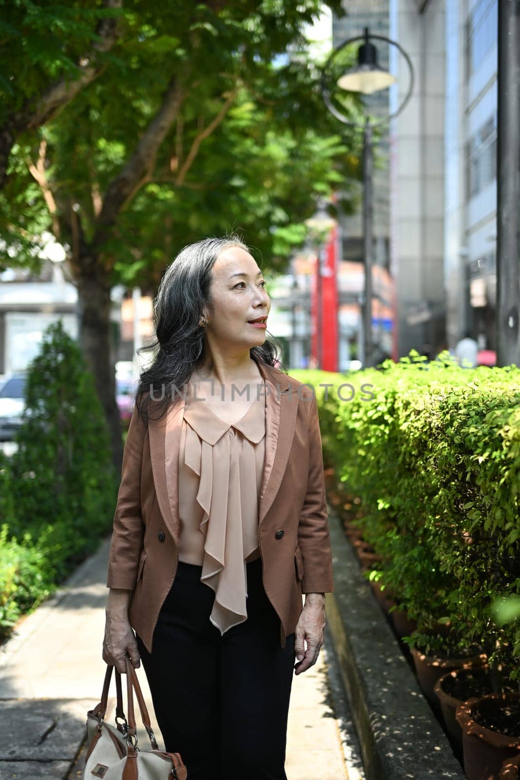 Positive mature businesswoman strolling through an urban park on beautiful day.
