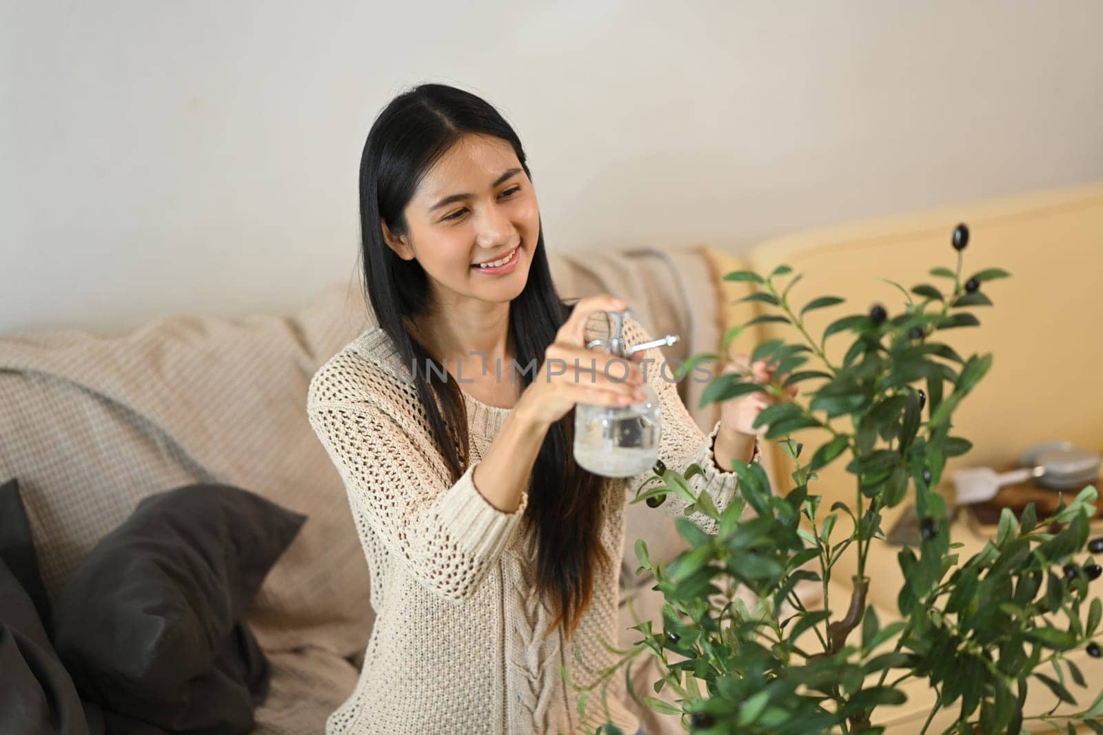 Beautiful young woman taking care and spraying water on houseplants with a bottle.