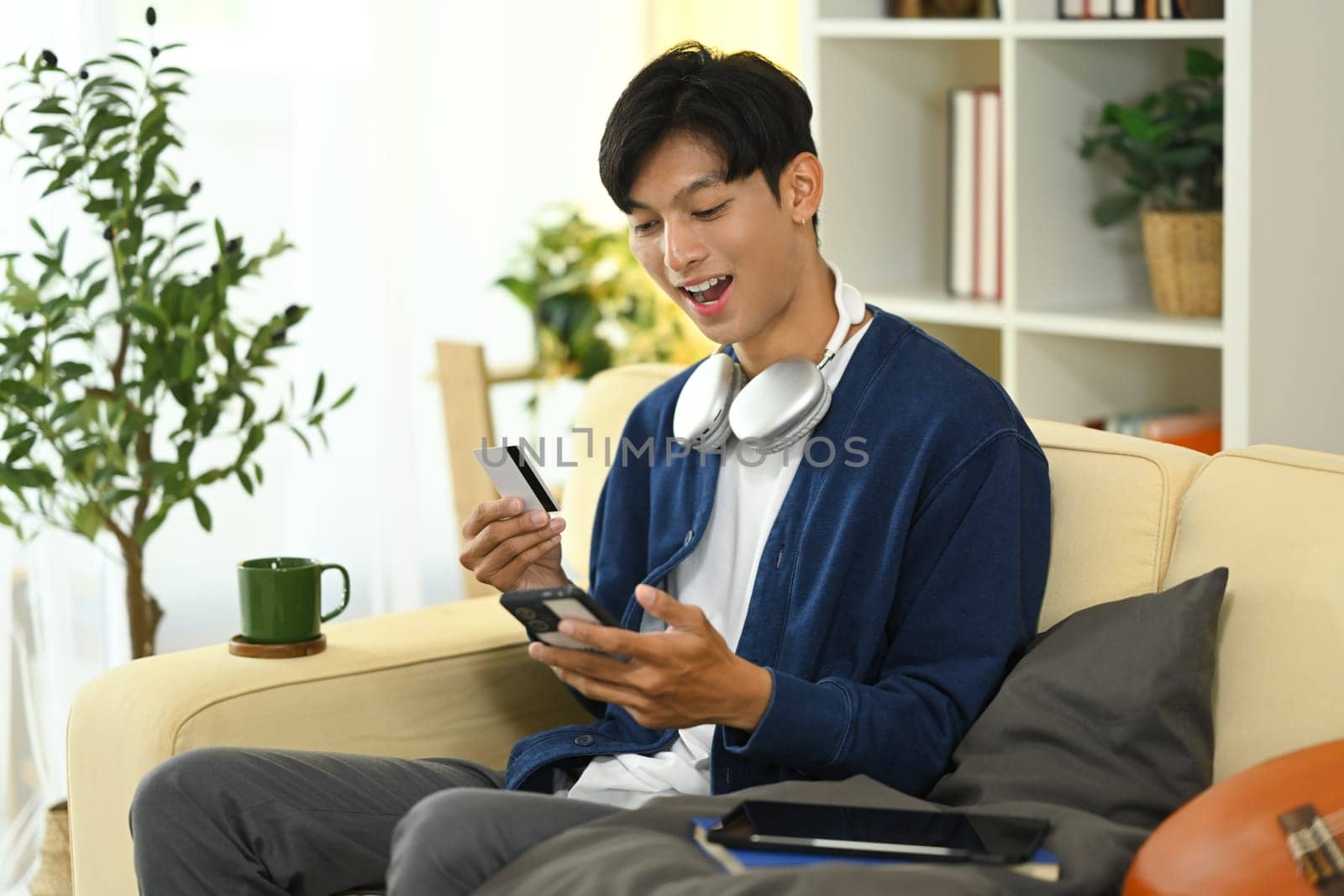 Excited asian man making an online purchase with smartphone and credit card.