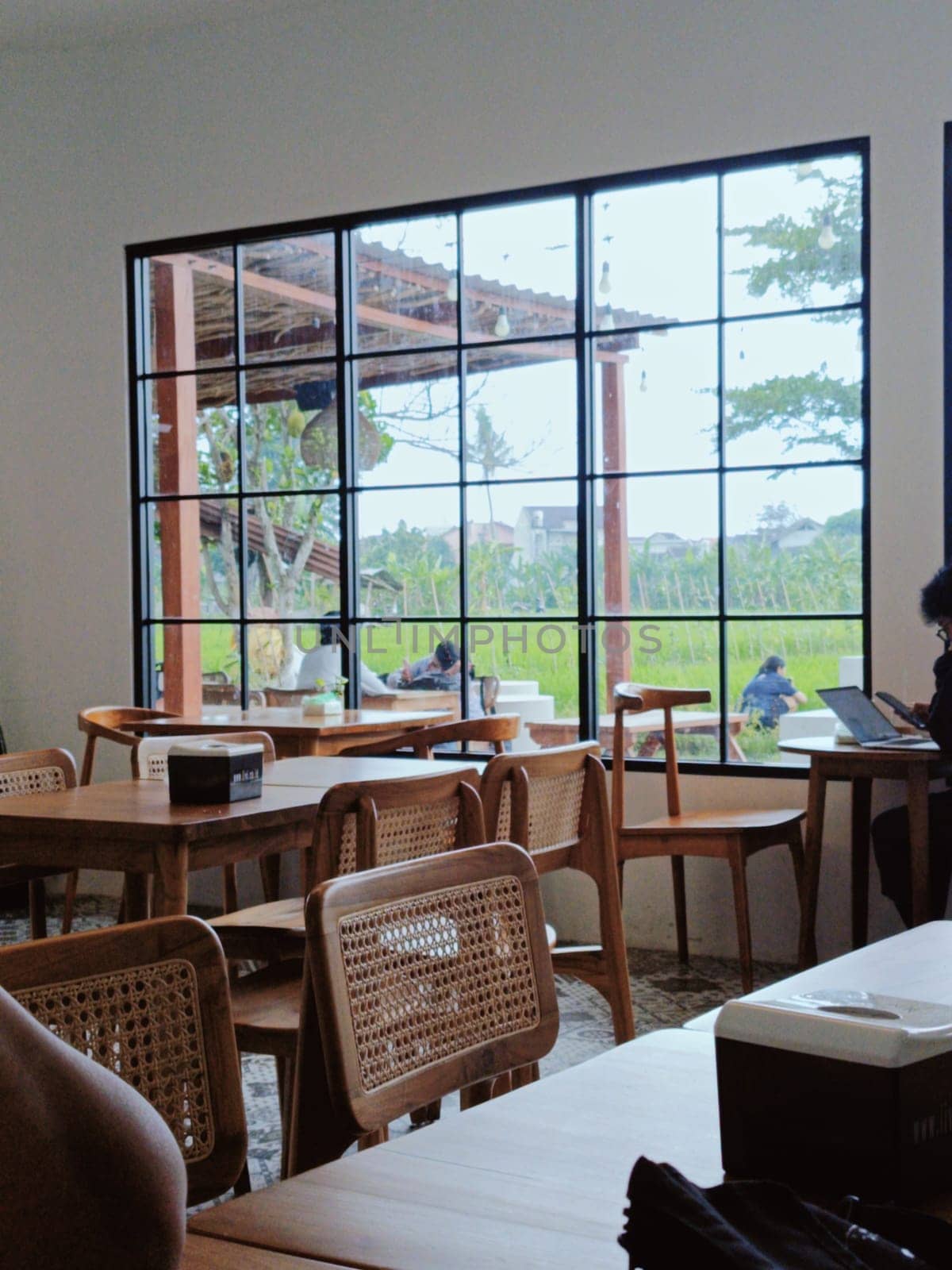 A cozy cafe interior featuring wooden furniture with a large window overlooking a serene garden. The peaceful atmosphere is ideal for relaxation and work.