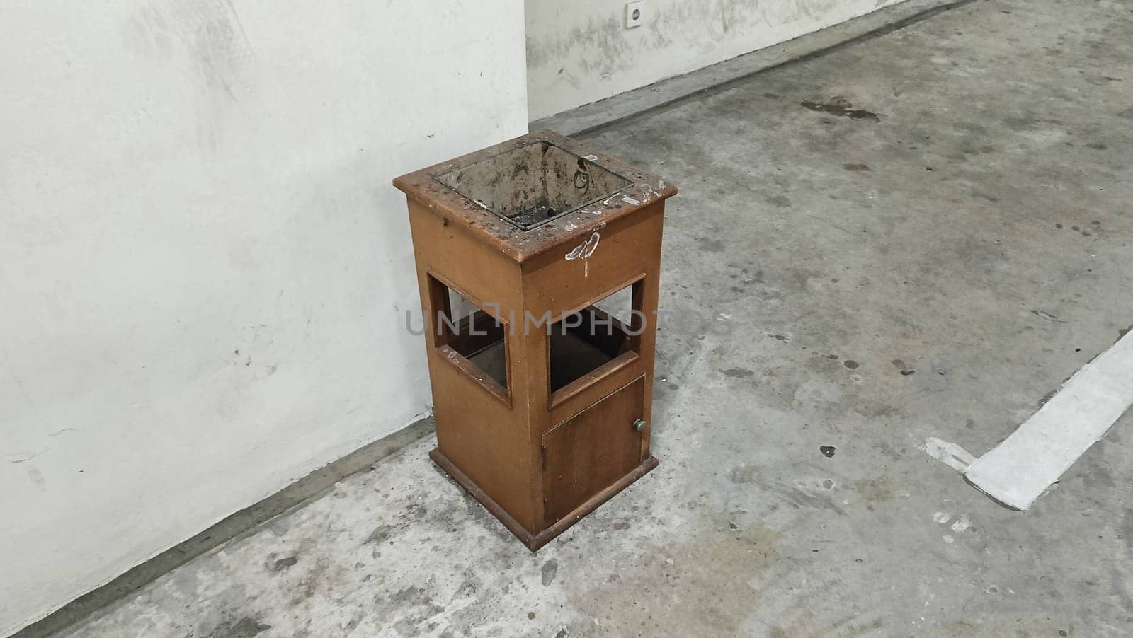 An old brown wooden drawer stands alone in a neglected concrete space, suggesting themes of abandonment and time. The industrial environment adds to the sense of decay and desolation.