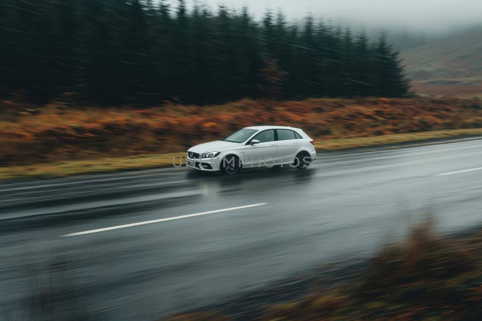 A fast-moving car creates a striking motion blur as it traverses an empty road surrounded by serene, foggy landscapes, embodying speed and freedom.