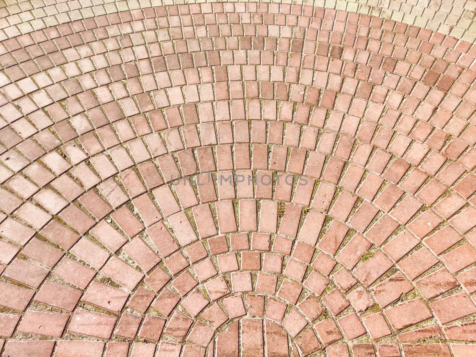 The ground is covered with a detailed arrangement of red bricks creating a circular pattern under the sunlight.
