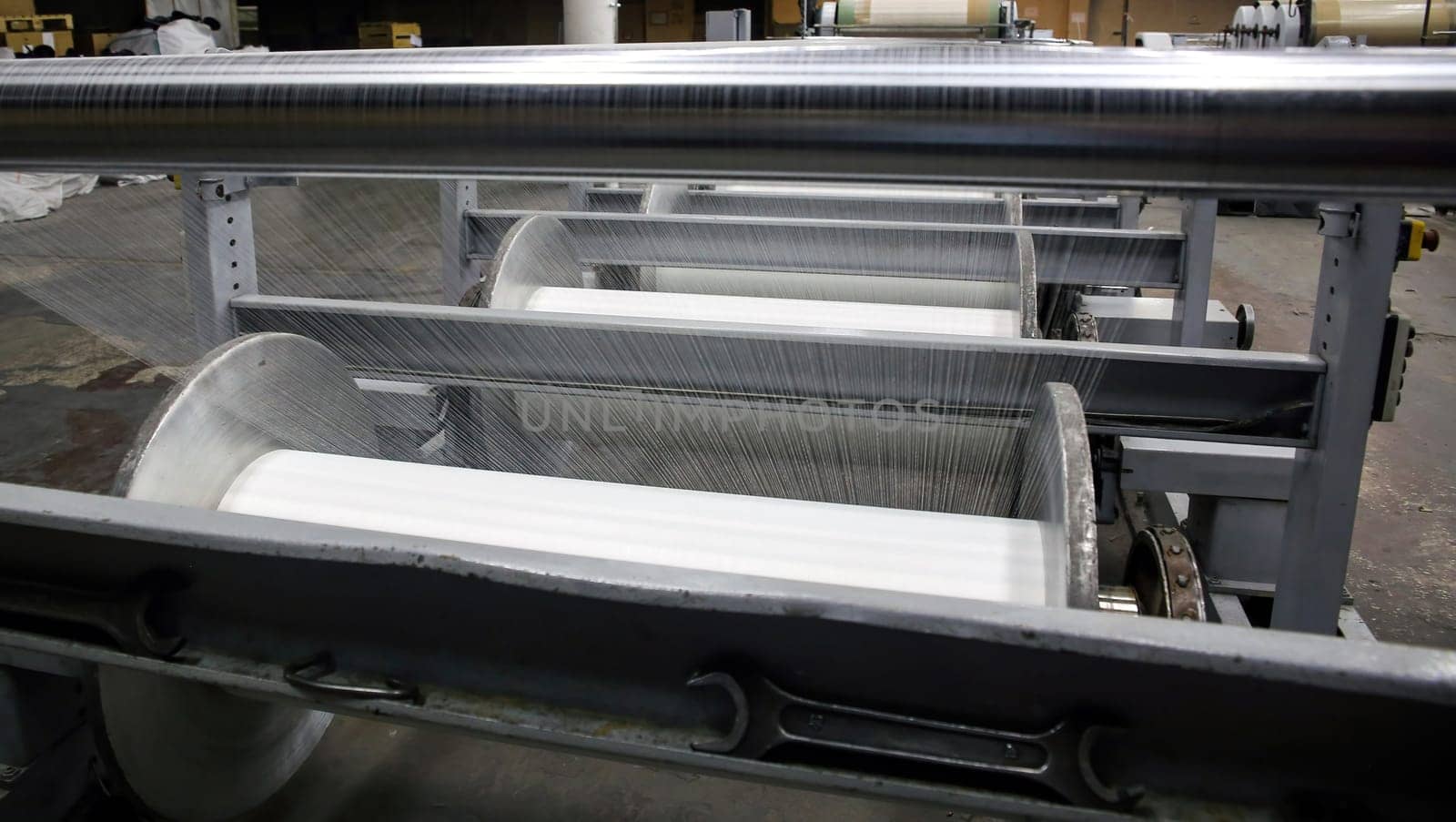 An industrial knitting machine in a textile factory with spools of white thread on a production line. Weaving fabric from yarn in a clean, well-lit manufacturing environment.