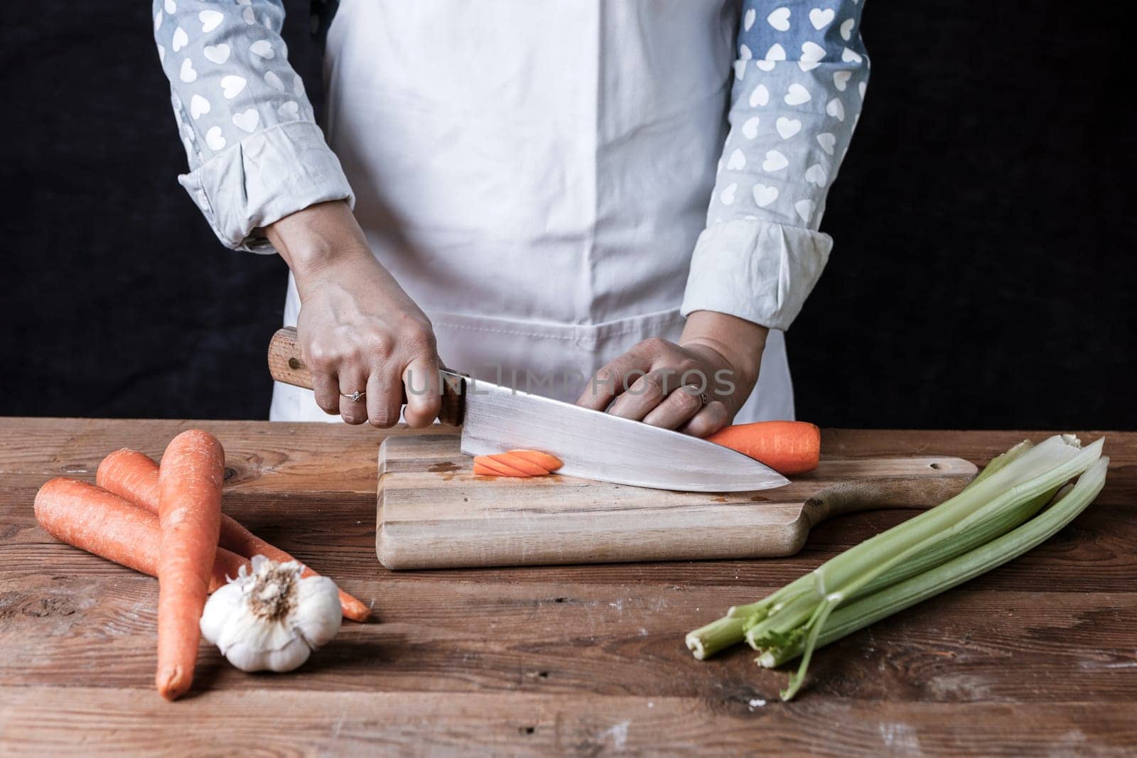 Cutting carrots on a cutting board with celery and garlic on the table.