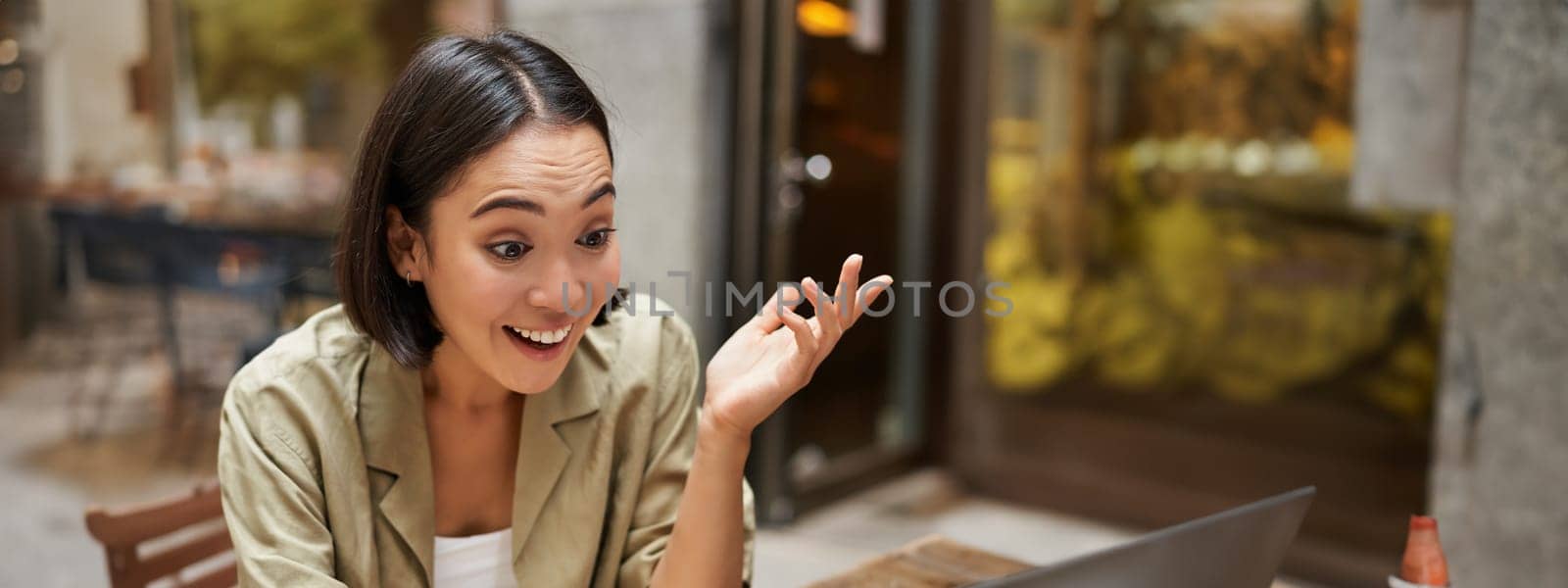 Vertical shot of young brunette girl chatting on video chat, having online meeting, talking to laptop, sitting in cafe by Benzoix