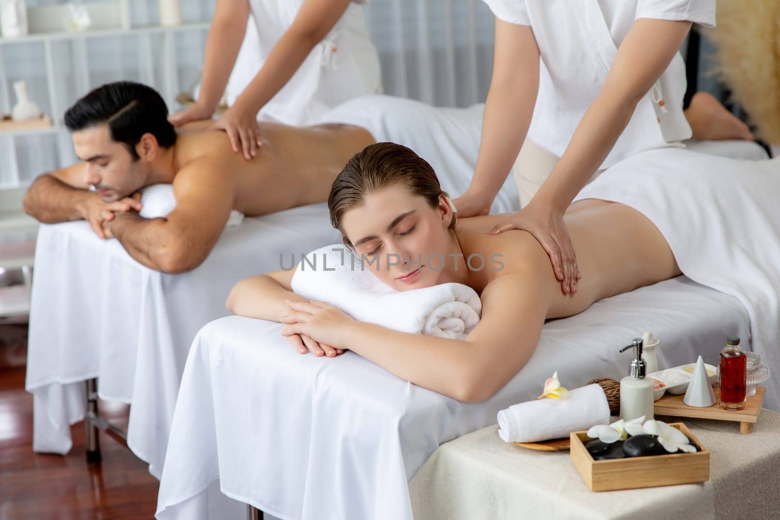 Caucasian couple customer enjoying relaxing anti-stress spa massage and pampering with beauty skin recreation leisure in day light ambient salon spa at luxury resort or hotel. Quiescent