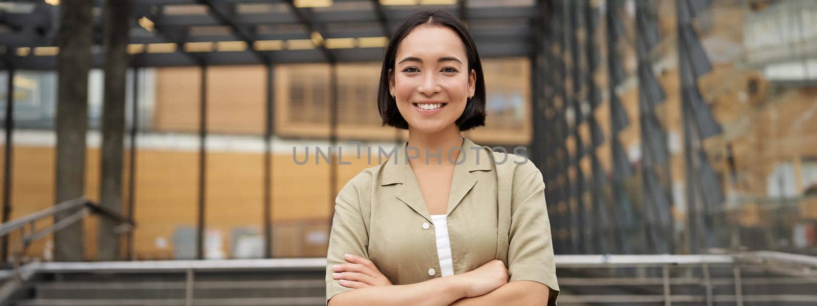 People. Portrait of confident korean girl, young student cross arms on chest, standing in power pose and smiling at camera.