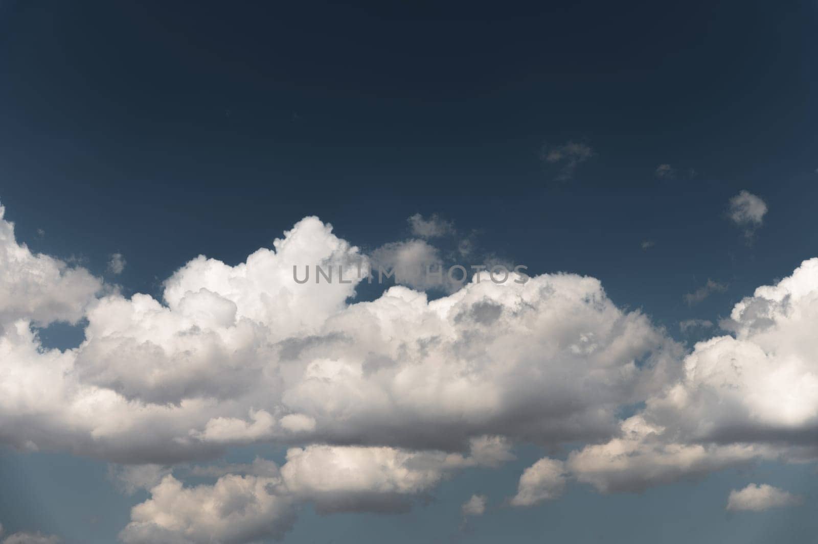 Part of the cloud is divided into large air clouds. White cumulus clouds against clear blue sky close up, cloudy sky background.
