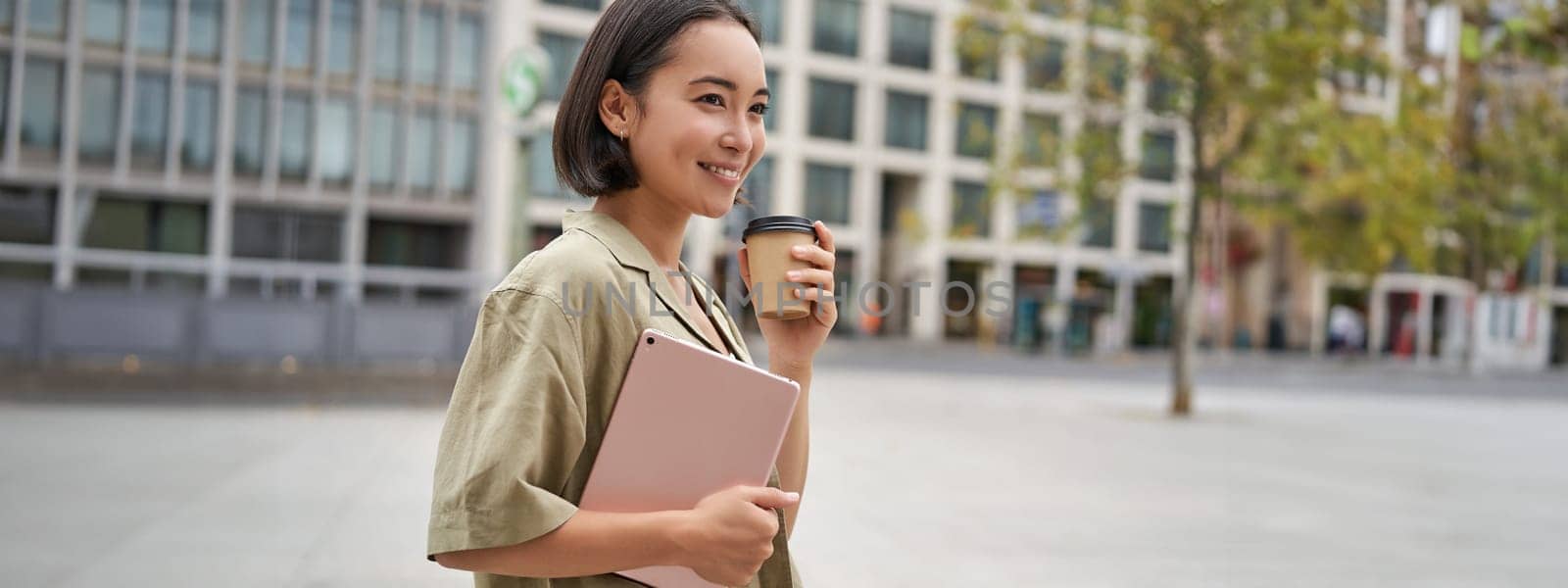 Portrait of asian girl with tablet, drinks coffee on street, walking in city centre by Benzoix