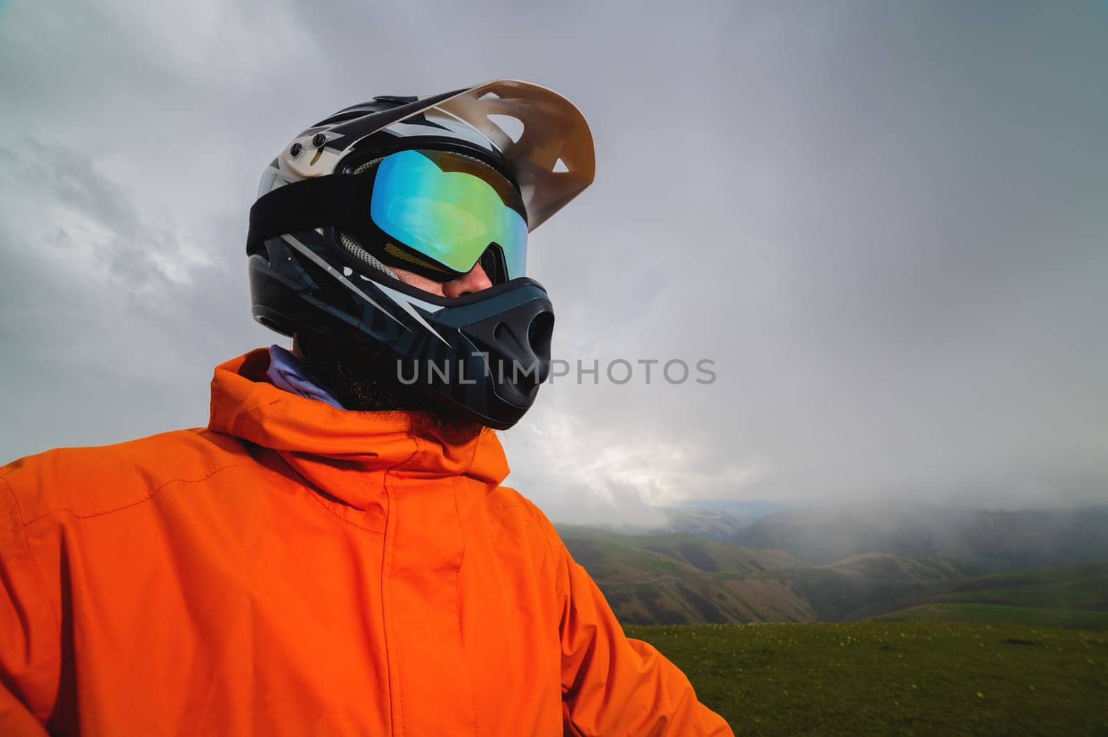 Portrait of a man in a protective sports helmet and reflective glasses. An athlete in full face in the mountains looks to the side.