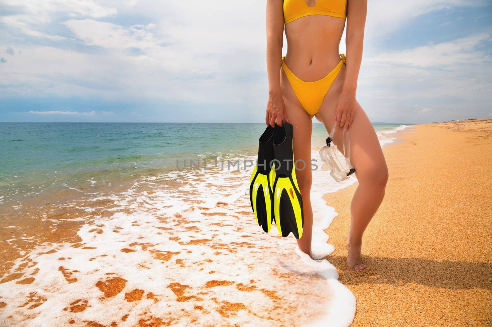 Sexy girl in a swimsuit with fins and a mask on the blue coast. Beautiful sporty woman on the beach with snorkeling equipment, healthy lifestyle or vacation concept.