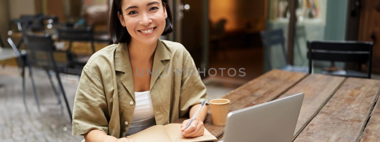 Portrait of young korean girl making notes, listening online meeting, lecture, looking at laptop screen, working remotely from cafe by Benzoix