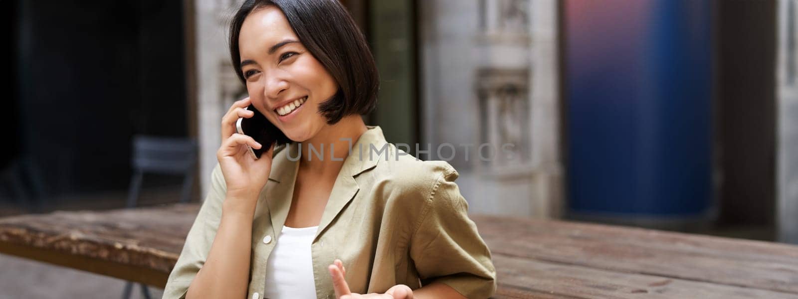 Young woman having conversation on mobile phone, sitting outdoors and making phone call, using smartphone, talking.