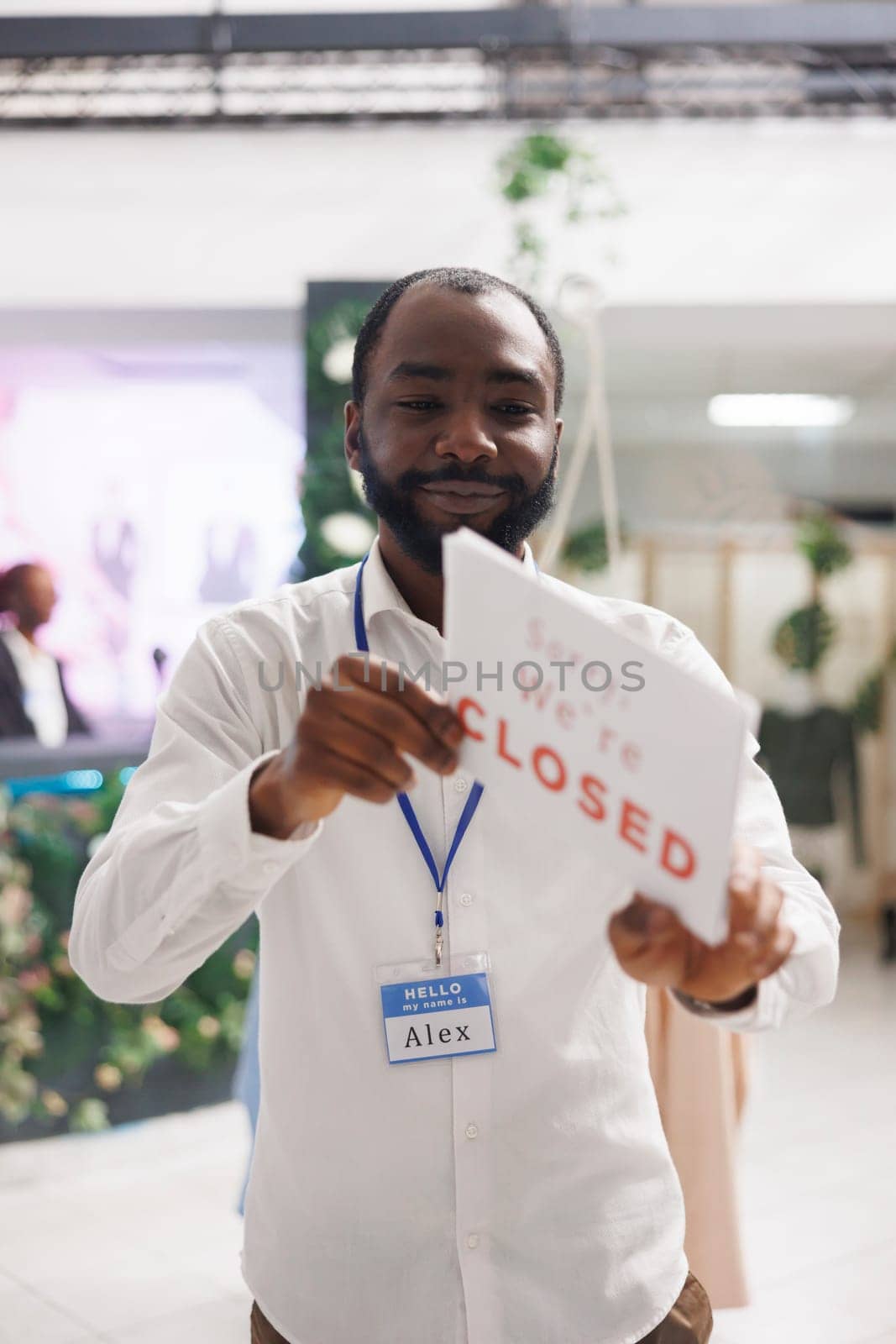 Clothing store smiling african american owner holding sorry we are closed sign. Fashion boutique cheerful man assistant hanging sign informing about end of business hours