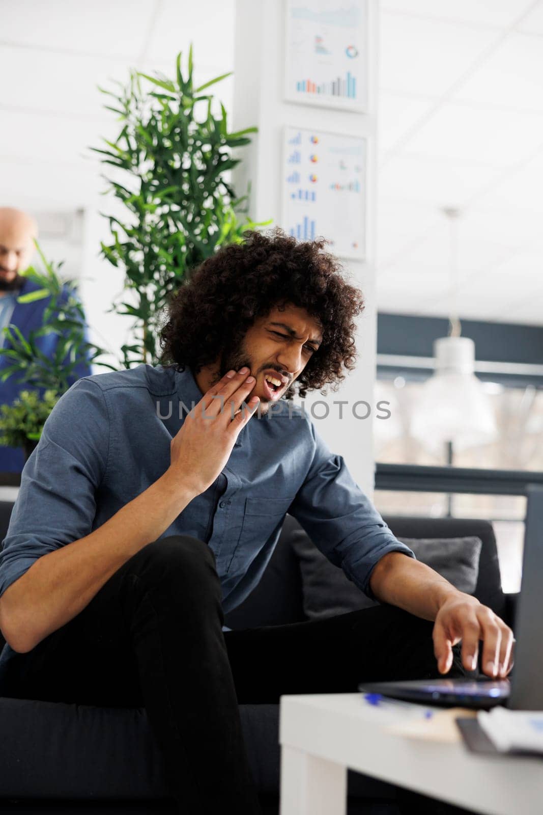 Executive manager having toothache while planning business development in start up office. Young arab company entrepreneur holding cheek and suffering from pain while working