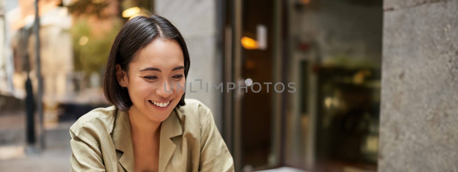 Smiling young woman working from cafe or co-working space, sitting with laptop, studying or doing homework, looking happy by Benzoix