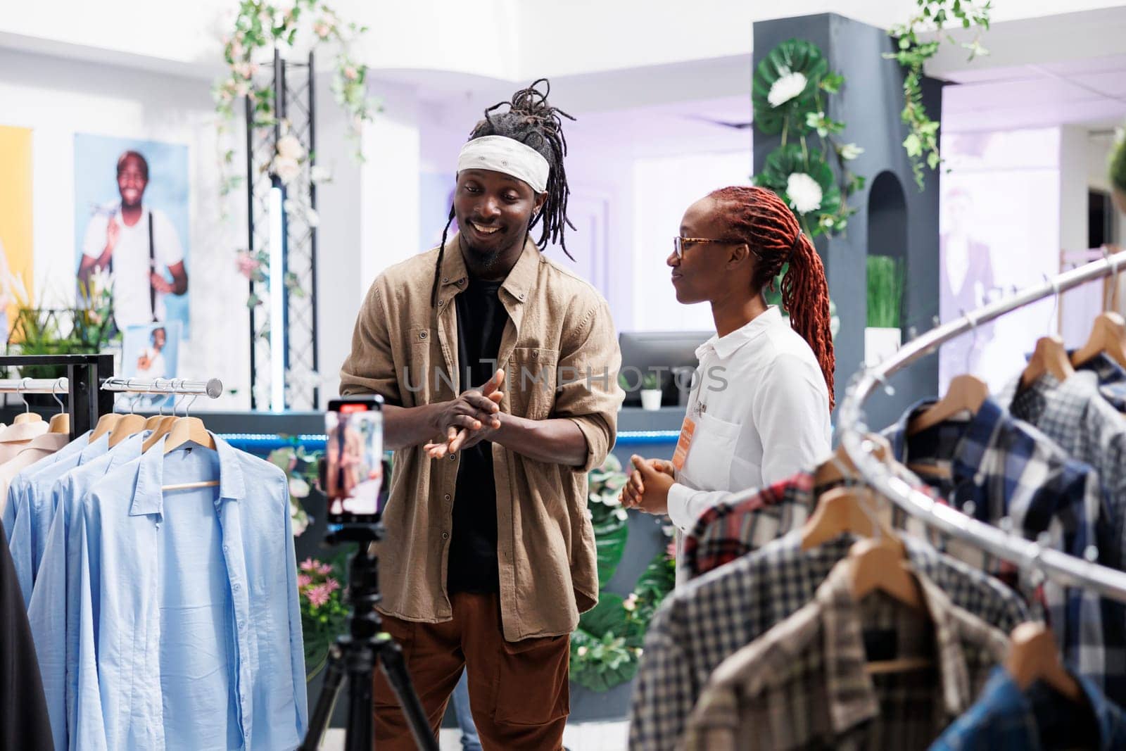 Influencer and clothing store assistant promoting fashion brand while recording video for social media. Blogger and boutique worker discussing trends while streaming in shopping mall