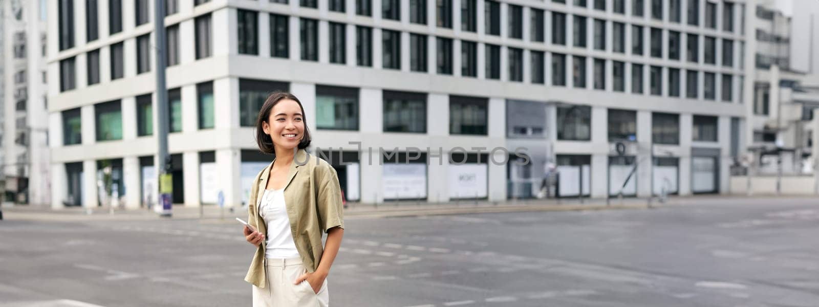 Woman smiling, standing with smartphone on street, waiting for taxi, checking mobile phone app by Benzoix