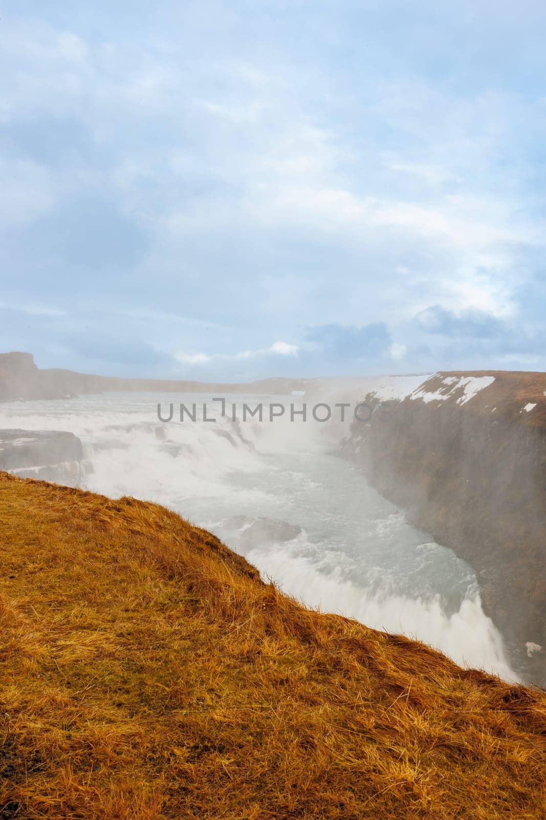 Gullfoss cascade in Iceland, consists of majestic river stream and untouched arctic nature. Nordic scenic route with huge waterfall and stream flowing alongside snow covered hills.