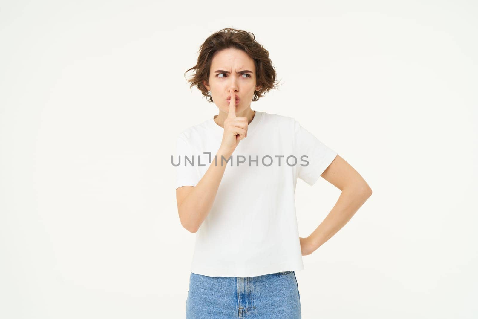 Image of brunette woman hiding secret, press finger to lips, hush, shush shh gesture, gossips, whispers, stands over white studio background by Benzoix