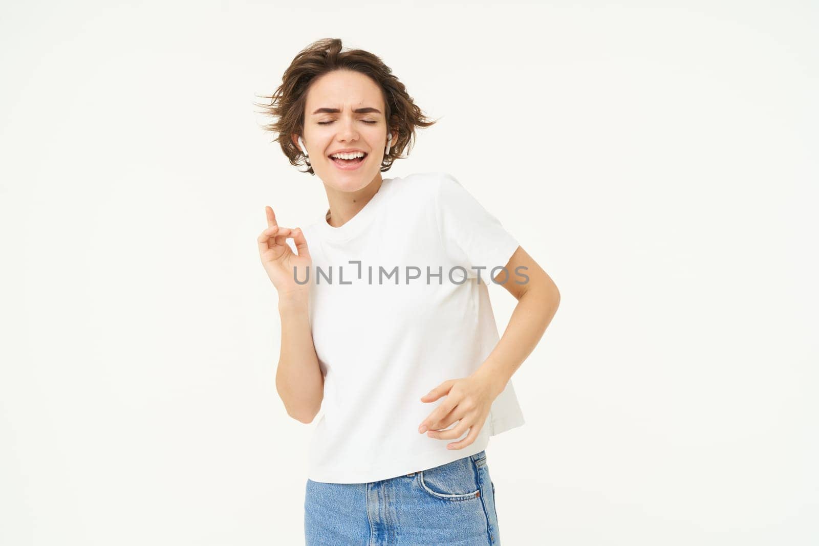 Portrait of happy young woman dancing, having fun, enjoying the music, posing over white studio background. Copy space