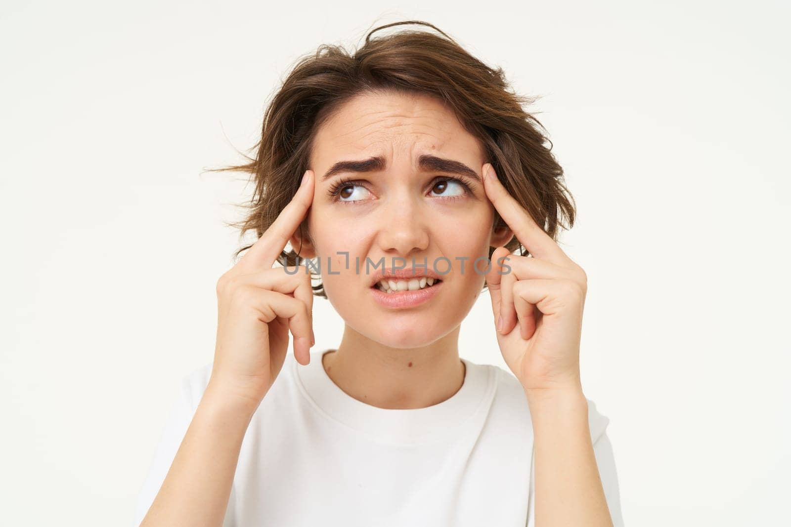 Image of woman touches her head temples, looks concerned, discomfort, has headache, tries to remember, thinking hard, standing over white studio background by Benzoix