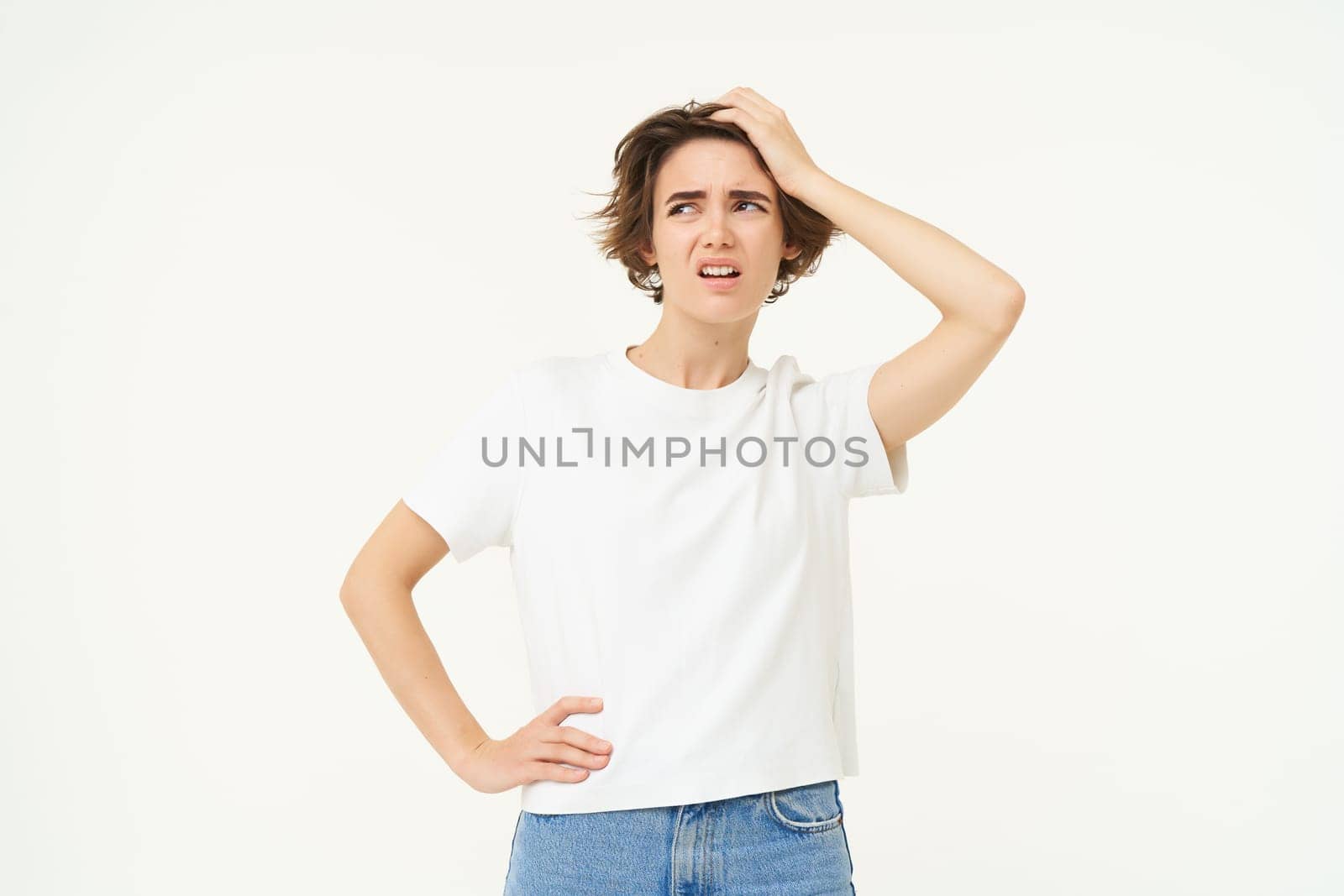 Portrait of woman looking troubled, slap her forehead, standing thoughtful and frowning, facing complicated problem, standing over white studio background.