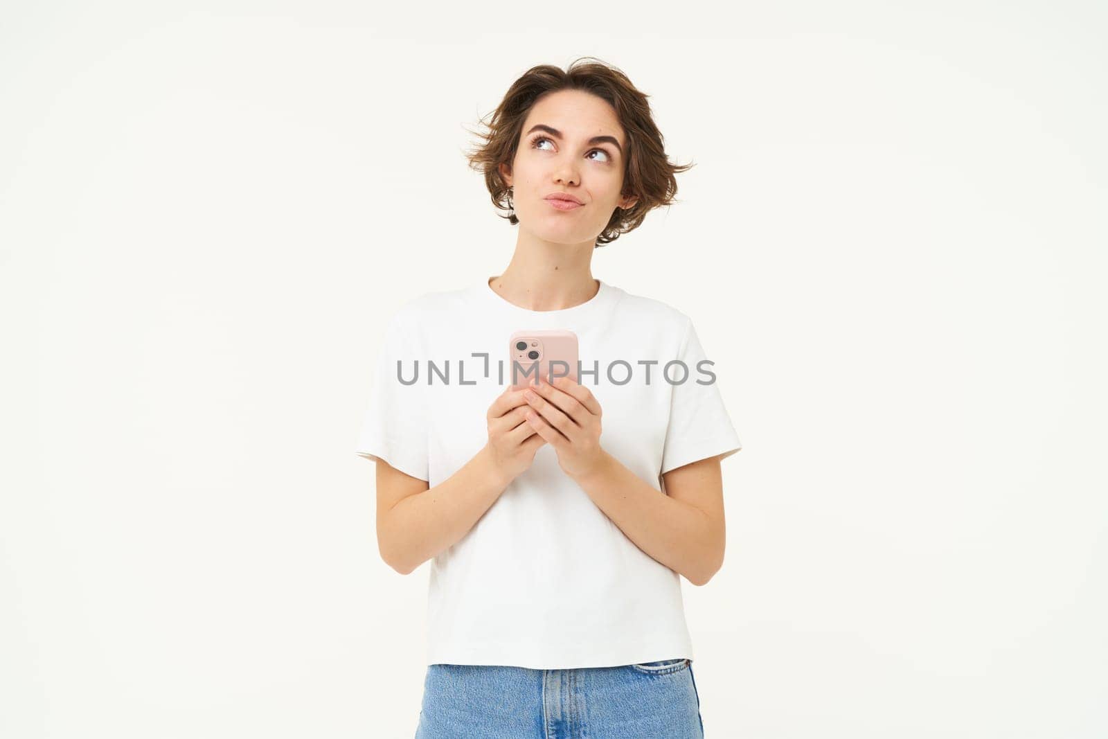 Portrait of woman thinking, using smartphone and looking thoughtful, making choice, deciding, standing isolated over white background by Benzoix