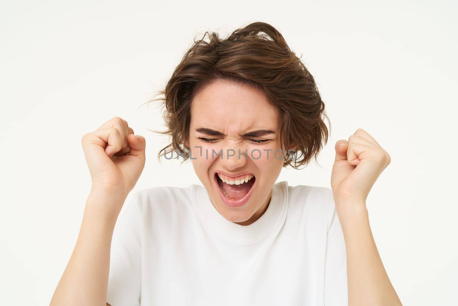 Close up of woman losing her temper, yelling, shouting and causing scene, jumping from frustration, clenching fists, standing over white background by Benzoix