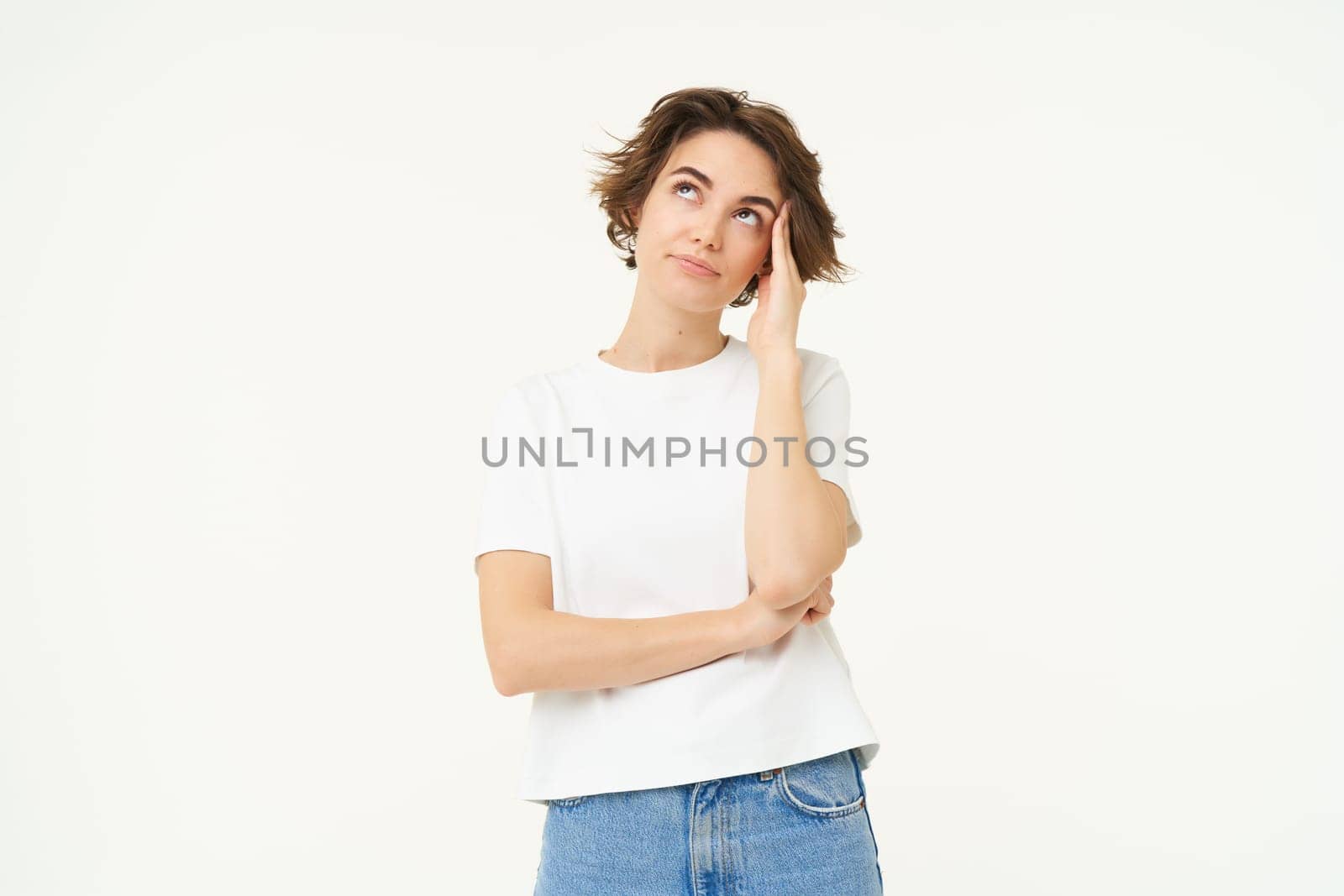 Portrait of puzzled woman, looking confused, staring up at ceiling, touches her head, standing tired against white background.